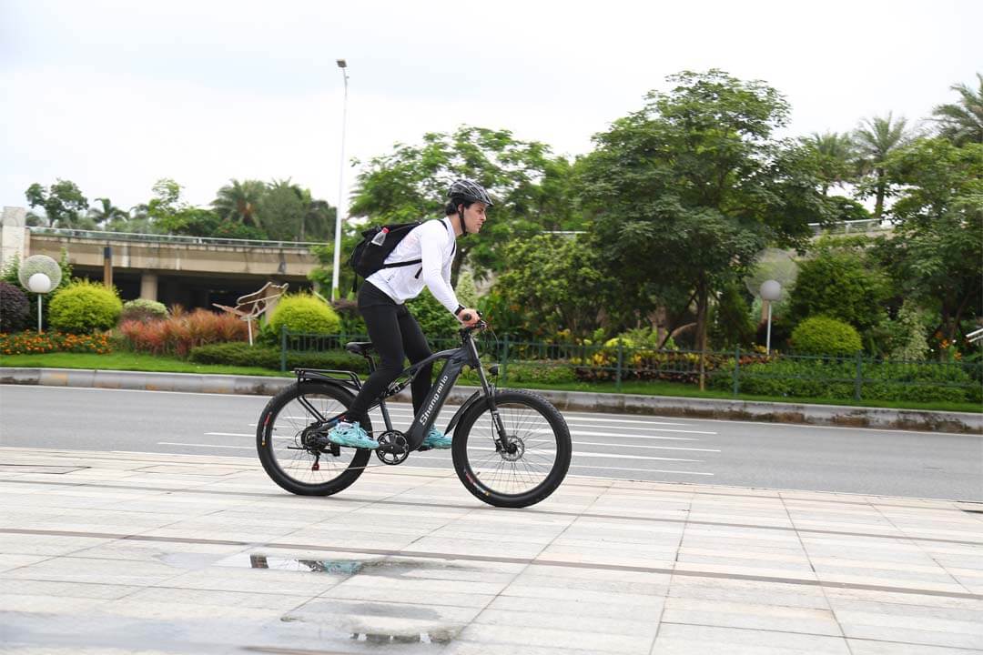 Un hombre monta una bicicleta de montaña eléctrica de suspensión total shengmilo mx05 en una carretera de la ciudad.