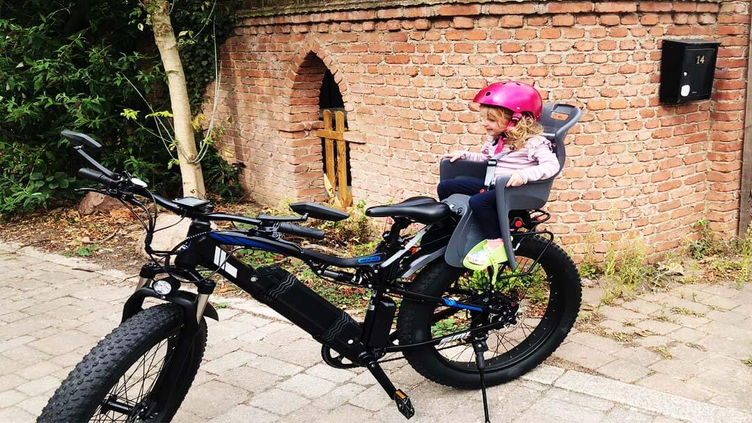 Child wearing child helmet sitting on bicycle child safety seat.